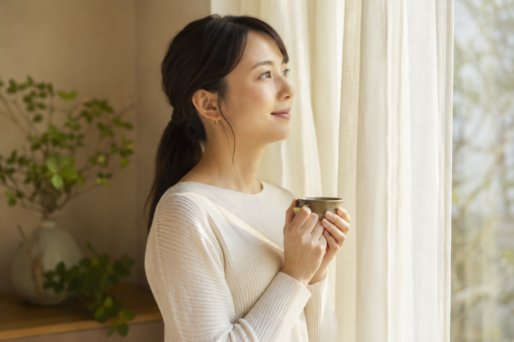 窓辺で穏やかな表情をたたずむ30代の日本人女性