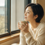 窓辺でコーヒーを手に物思いにふける30代の日本人女性