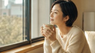 窓辺でコーヒーを手に物思いにふける30代の日本人女性
